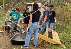 Female students from St. James school are mixing concrete and placing it in a hole they dug